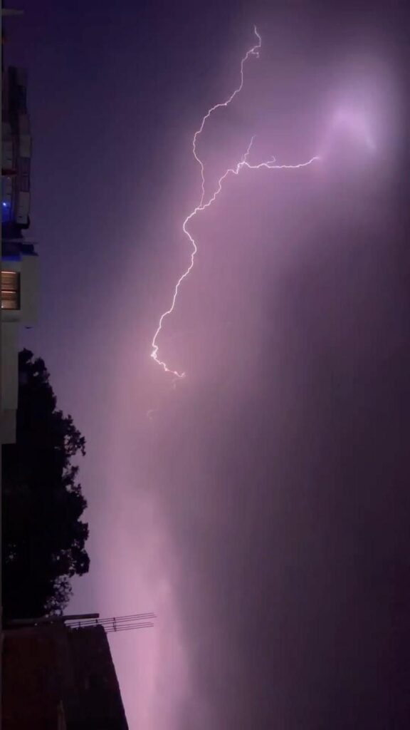 काले बादलों, तेज हवा और बारिश के बीच सड़क और पेड़ों का दृश्य, जो मौसम के खराब हालात को दर्शाता है