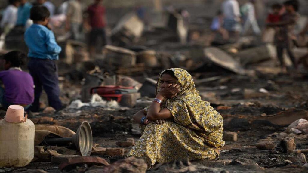 दिल्ली के रोहिणी क्षेत्र में झुग्गियों में लगी आग के बाद जले हुए ढांचे और राहत कार्य करते दमकलकर्मी दिखाई दे रहे हैं।